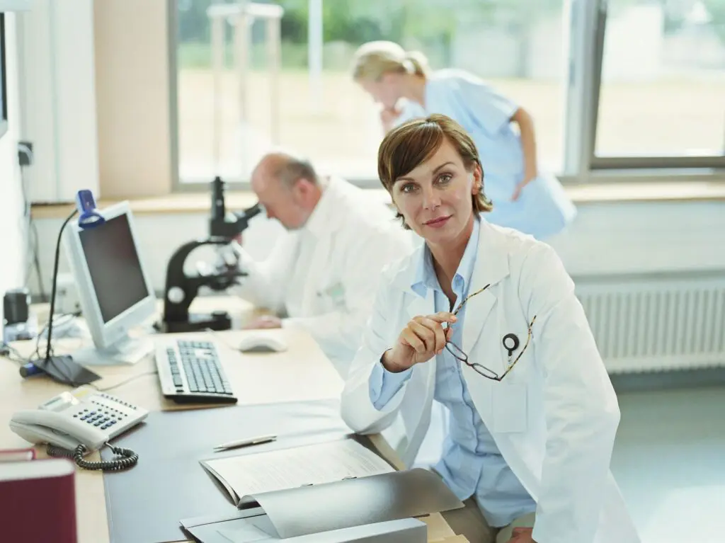 A woman in white lab coat sitting at a table.